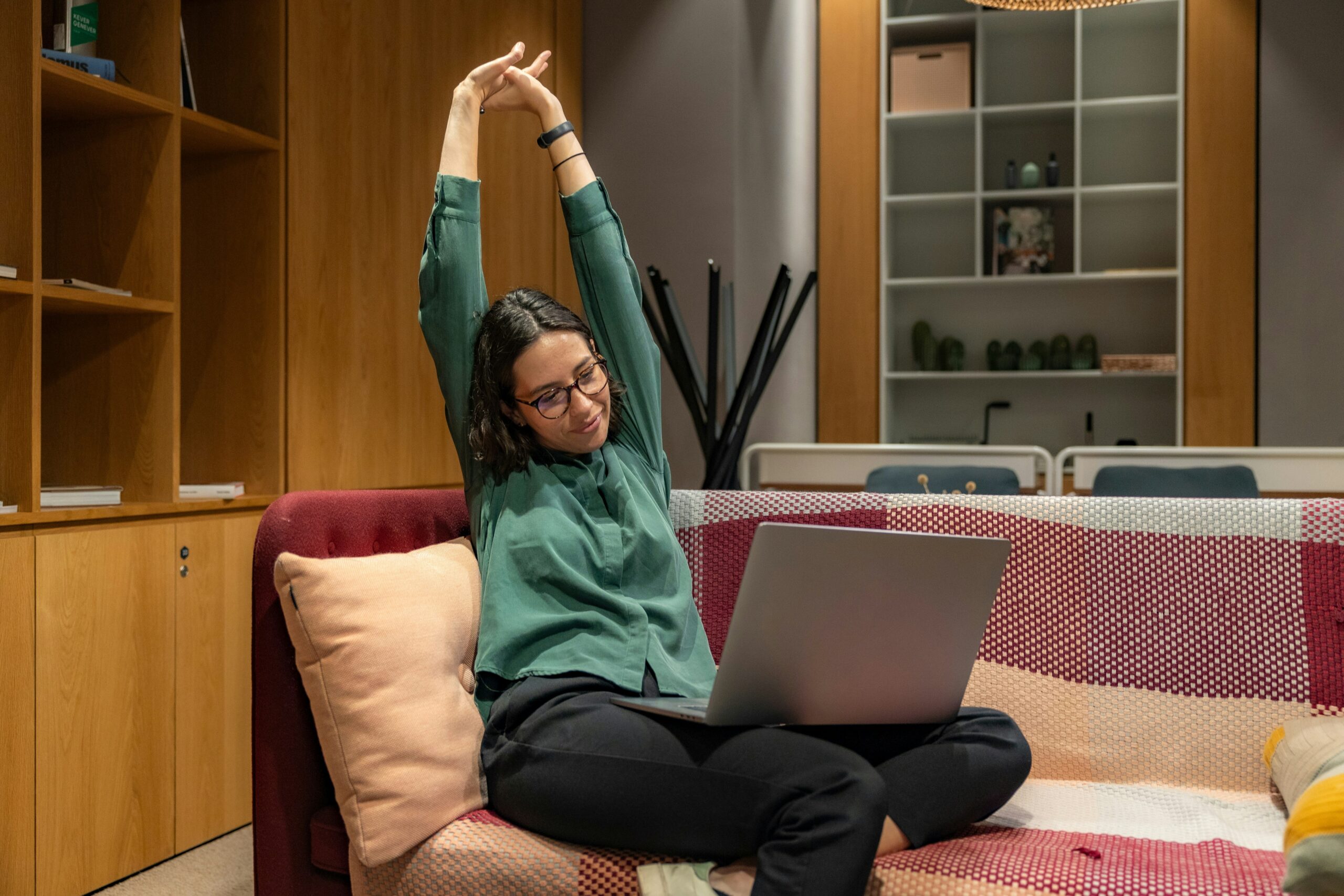 A woman demonstrating the spine stretch exercise, sitting upright on a yoga mat, reaching her hands toward her feet.